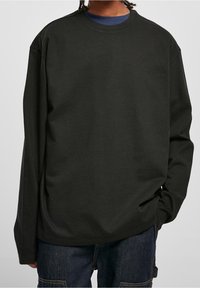 Black long-sleeve t-shirt in cotton with a crew neckline, relaxed fit, and dropped shoulder seams, worn over a navy shirt.