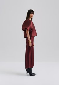 Robe en satin bordeaux avec un haut cropped boxy à manches bouffantes et une jupe ajustée. Bottes à talons aiguilles noires et bracelets en or comme accessoires.