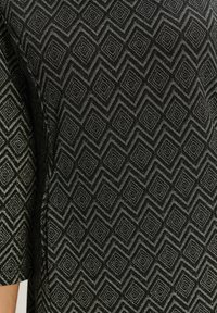 Čierny textil s geometrickým vzorom diamantov a cik-cak, s textúrovaným povrchom a krátkymi rukávmi.