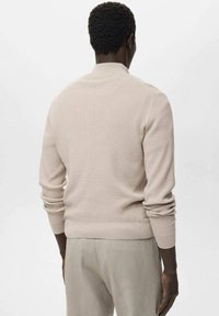 Jersey de punto de canalé beige con un cuello redondo ceñido y mangas largas. Presenta un diseño texturizado y una cintura ajustada.