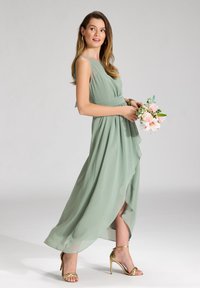 Abito in chiffon verde menta con un design fluido, spacco fino al ginocchio e vita aderente. Abbinato a sandali con tacco alto e fasce dorate.