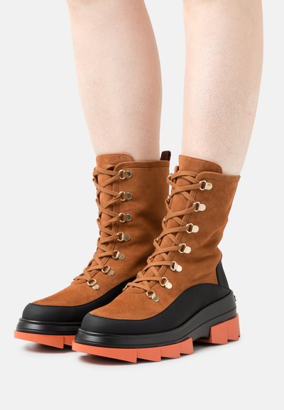 Tan suede ankle boots with black rubber soles and orange platform. Features gold eyelets and laces for secure fastening.