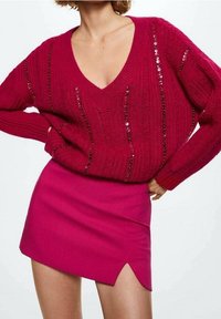 Fuksia neulepaita V-puolella, koristeltu helmiäisillä, yhdistetty istuvaan vaaleanpunaiseen mini-hameseen, jossa on sivuaukko.