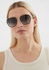 Zwarte en grijze gradient oversized hexagonale zonnebril met metalen accenten. Heeft een robuuste montuur en getinte glazen, wat zorgt voor een gedurfde uitstraling.
