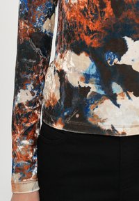 Langärmliges Hemd aus mehrfarbigem, strukturiertem Stoff mit abstrakten Mustern in Orange, Blau und Creme, kombiniert mit schwarzen Hosen.