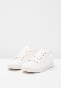 Vita sneakers i syntetmaterial. Funktioner inkluderar snörningsdesign, roséguldiga accenter, perforerade detaljer och texturerad gummisula.