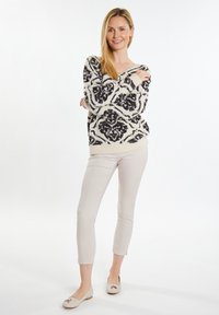 Cremefarbener Pullover mit schwarzem Blumenmuster, leichtes Material, kombiniert mit hellbeigen, figurbetonten Hosen und nude-farbenen Ballerinas. Einfaches, lässiges Outfit.
