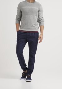 Grijze gebreide sweater met een textuurpaneel, gecombineerd met marineblauwe joggers en marineblauwe sneakers met witte zolen en bruine veters.