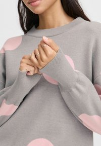 Light grey sweater with oversized pink polka dots, ribbed cuffs, and a crew neckline. Soft texture and relaxed fit.