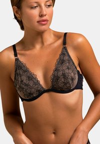 Soutien-gorge triangle en dentelle florale noire avec des bonnets transparents, des bretelles ajustables et une bande sous poitrine lisse pour le soutien. Détails floraux embellis sur l'ensemble.