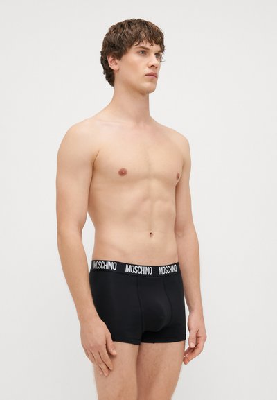 Mustad mustra musta poksi, millel on pehme tekstuur ja kontrastne valge logo rihm. Kujundus on sügavalt talje piirkonda ning ulatub keskkohast reie keskpaiku.