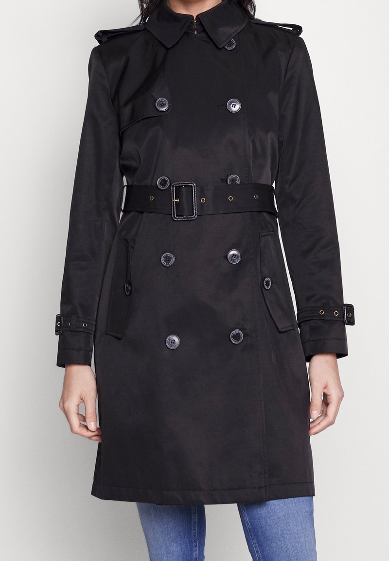 Svart trenchcoat med dubbelknäppt design, stora knappar, bälte i midjan, axelremmar och sidofickor. Slät tygtextur.