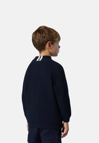 Suéter de punto azul marino oscuro con textura de canalé y cuello redondo. Presenta un detalle de franjas blancas en la parte de atrás del cuello.