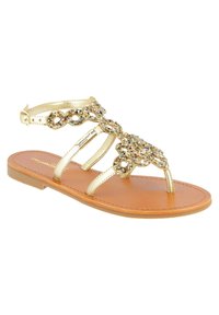 Gold metallic sandal with beaded embellishments, flat sole, adjustable ankle strap, and tan footbed. Open-toe design and minimalist style.