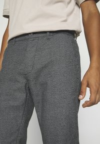 Gray plaid trousers made of textured fabric. Features a fitted design, front pockets, and a subtle check pattern with dark accents.