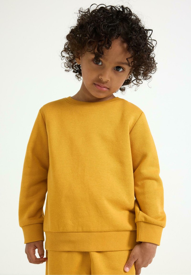 Gelbes Baumwoll-Sweatshirt mit rundem Halsausschnitt, gerippten Bündchen und lockerer Passform, das eine glatte Textur und ein minimales Design aufweist.