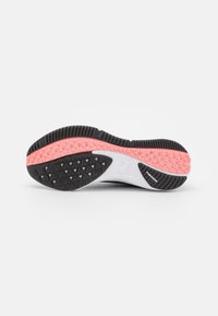 Suela de zapatilla deportiva en blanco y negro con una parte inferior de goma texturizada; cuenta con acentos en rosa y un patrón de banda de rodadura triangular para mayor agarre.