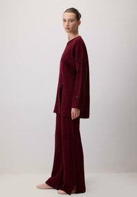 Burgundowa dzianinowa stylizacja z prążkowanym wzorem, oversize'owy kardigan z guzikami oraz szerokie spodnie z bocznymi rozcięciami. Miękka tekstura.