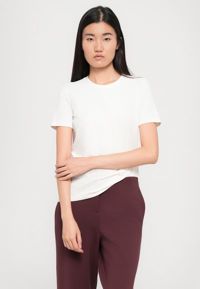 Weißes kurzärmliges T-Shirt aus weichem Stoff, mit Rundhalsausschnitt und lässiger Passform, kombiniert mit dunkelrotbraunen Hosen.