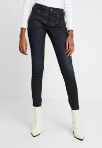 Svarta slim fit-jeans med glänsande yta, som har dragkedjefickor och en figurnära design, matchade med krämfärgade spetsiga ankelstövlar.