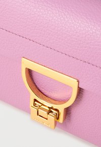 Pink leather handbag featuring a gold-tone hardware clasp and a textured surface. Notable details include a rounded handle and contrasting stitching.