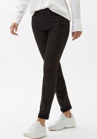 Černé kostkované džíny s úzkým střihem a ohrnutými nohavicemi, doplněné o bílé tenisky. Tkanina vypadá texturovaně a odolně.