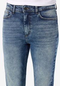 Blå denimjeans med falmet finish, fem-lommet design og kontrasterende sømmer. Har en metallknapp i midjen.