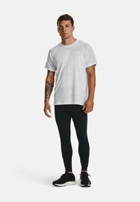Maglietta sportiva bianca a maniche corte, abbinata a leggings neri e scarpe da running nere. Presenta un design semplice e una texture liscia.