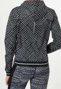 Woman wearing a black and white geometric patterned hooded jacket and black and white textured leggings, shown from the back.