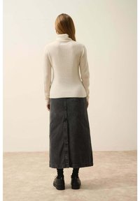 Krémový žebrovaný rolák spárovaný s dlouhou šedou džínovou sukní s rozparkem vzadu, nošený s černými platformovými botami.