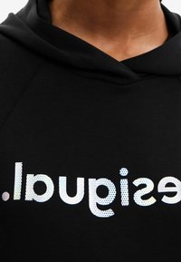 Felpa nera con cappuccio, caratterizzata da testo riflettente bianco che legge "seguisdil" in un carattere bold e arrotondato. Texture liscia e design casual.