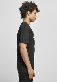 Svart bomull T-skjorte med grafisk trykk foran, kortermet og klassisk rund hals. Modellen står i profil.