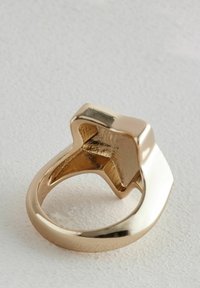 Anello dorato con una parte superiore a forma di stella con superficie liscia, banda arrotondata e finitura lucida. L'interno presenta una superficie dorata texturizzata.
