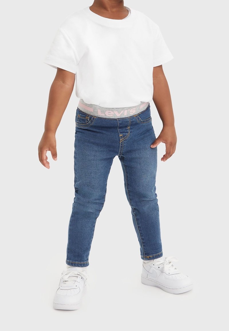 Vit t-shirt med kort ärm, ljusblå denimjeans med en grå och rosa Levi's midja, samt vita sneakers med snörning.