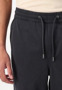 Graue sportliche Jogginghosen mit elastischem Bund, Zugbandakzenten und seitlichen Taschen. Der Stoff hat eine glatte, leichte Textur.