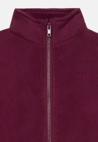 Burgunderfarget fleecejakke med høy krage, sentral glidelås og lite brodert "only"-logo på venstre bryst.