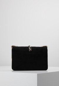 Borsa a tracolla in suede nero con catena, forma rettangolare, texture liscia, hardware centrale in tono argento e design minimalista.