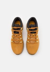 Scarpe da trekking marroni con parte superiore in suede beige, fodera in tessuto nera, lacci arancioni e accessori in tonalità oro. Punta rotonda e collo imbottito.