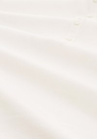 Vitt bomullspolotröja med en mjuk textur, dekorerad med knappdetaljer och ett fint ribbat mönster.