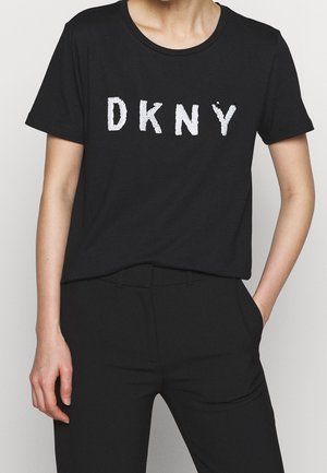 Black cotton t-shirt featuring white "DKNY" lettering on the front. Short sleeves, round neckline, relaxed fit, paired with black pants.