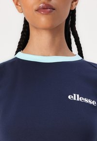 Námornícka tričko s svetlomodrým rebrovaným okrúhlym výstrihom, s bielym vyšitým logom "ellesse" na prednej strane. Hladká bavlnená tkanina, bežný strih.
