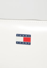 White sleek pouch featuring a zipper closure and a Tommy Jeans logo in blue, red, and white on the front. Smooth texture and minimalist design.