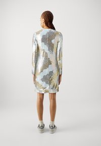 Dlouhé šaty s dlouhým rukávem vyrobené z barevných flitrů, obsahující směs stříbrné, zlaté a pastelových odstínů; zapínání na zip na zadní straně; délka po kolena.