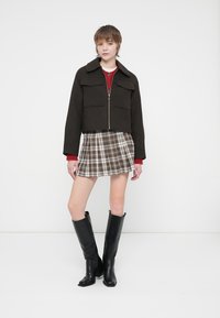 Zwarte cropped jack met twee borstzakken, rode trui, geruite rok en zwarte knie-hoge laarzen. Soepele textuur en gestructureerd ontwerp.