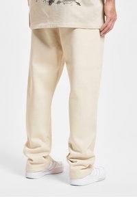Beige sweatpants med en afslappet pasform, lavet af blødt stof, har mansjetterede kanter og en glat overflade, parret med hvide sneakers.