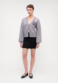 Cardigan gri tricotat cu un accent de design în spirală, mâneci supradimensionate și decolteu rotund, asortat cu o fustă neagră conică și pantofi plata.