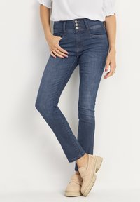 Mörkblå skinny jeans med hög midja, med tre framknäppningar, fem fickor och en jämn denimtextur. Bärs med beiga slip-on skor.