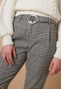 Zwart-witte ginghampatroon broeken met een hoge taille, voorzien van een zilveren ronde riemgesp en een relaxte pasvorm. Getextureerde stof zichtbaar.