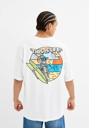Camiseta blanca de manga corta con un estampado gráfico de un esqueleto con una tabla de surf frente a una escena de playa con colores de atardecer.