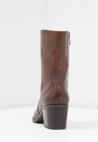 Hnědá kožená kotníková bota s kulatou špičkou, bočním zipem a zúženým podpatkem. Disponuje hladkým povrchem a jemnými švy.